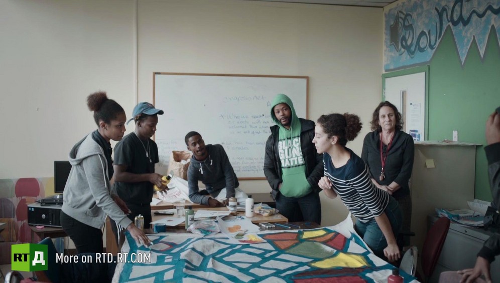 African American students stand around the large sheet of paper they are painting during art class at YESPHilly second chance high school in Philadelphia, USA, while being wacthed by school founder Taylor Frome and Black Guns Matter activist Maj Toure. Still taken from RTD documentary Black Lives 5. Agents of Change