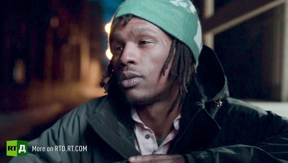 Head and shoulders of young African American male wearing a green hat. Taken at nightime in the street. Still taken from RTD Documentary film Black Lives 6. Illusion about single-parent families and teenage parenthood in Black America.