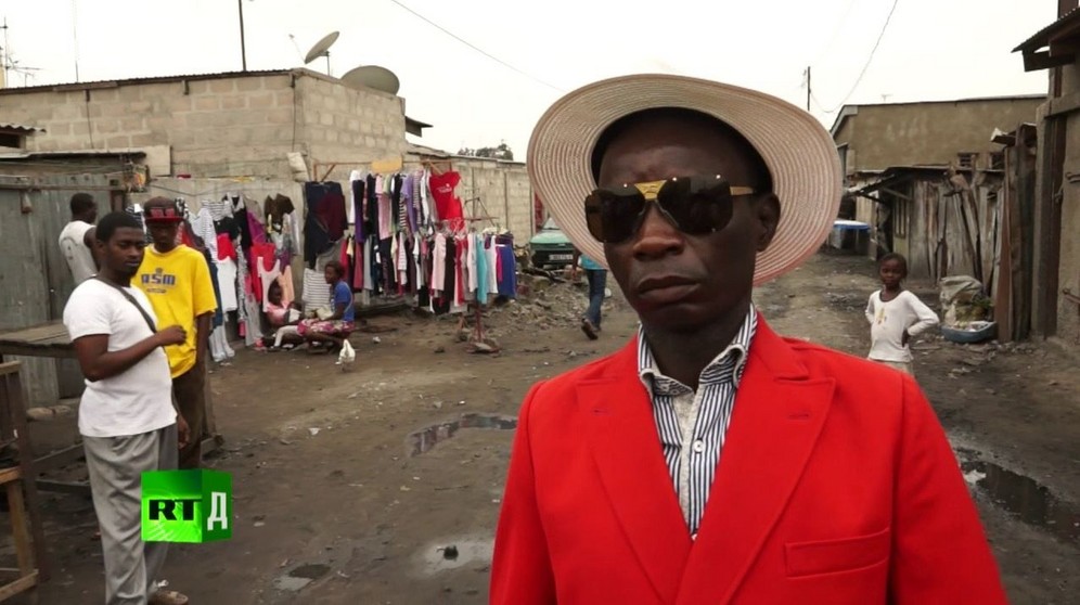Maxime Dutoit, a famous Congo Sapeur, wearing a red jacket and straw hat on streets of Brazzaville. Screenshot taken from RTD documentary Congo Dandies.