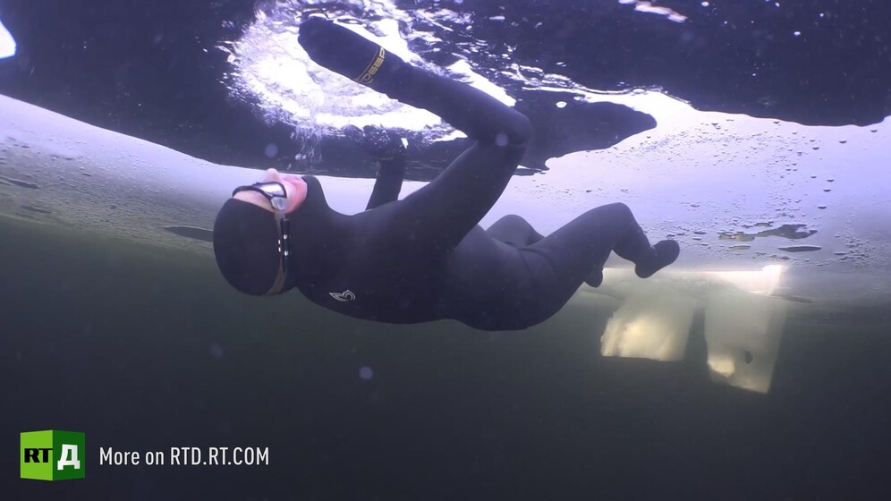 Freediver Andrey Matvenko surrounded by support team emerges from the ice-covered White Sea, Russia. Still taken from RTD documentary Freeze Divers.